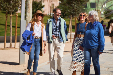 Four friends in their 60s strolling through a city square on a sunny day.