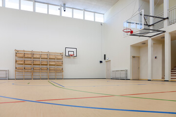 Indoor basketball court at a school. Wooden floor and marked court, a hoop and backboard.