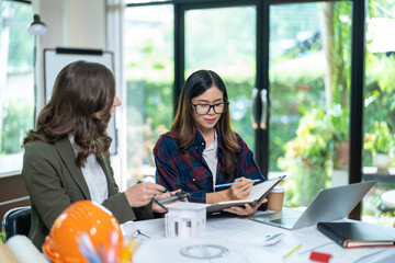 Concept of engineering consulting, Two female engineers discussing about model of building together; Two female architects are studying blueprint of building house.