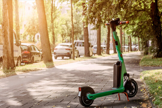 Electric Scooter for Rental on Sidewalk by Road with Many Cars in Green City. Electric Ride Sharing E Scooter. 
