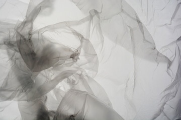 Close up picture on a plastic transparent cellophane bag on white background. The texture looks blank and shiny. The plastic surface is wrinkly and tattered making abstract pattern.