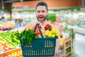 Man with shopping basket full of vegetables and fruits. Middle aged millennial man in a food store. Supermarket shopping and grocery shop concept. Man man 40s with shopping basket.