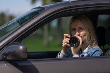 Fototapeta na wymiar Woman with a camera sits in a car and takes pictures with a professional camera, a private detective or a paparazzi spy. Journalist is looking for sensations and follows celebrities.