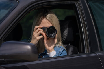 Young blonde woman takes pictures sitting in a car. Concept of journalism, detective, papparation