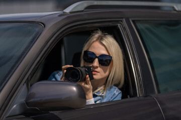 Fototapeta na wymiar Paparazzi woman or girl sits in her car and takes pictures of famous person. Spy with camera in car. Private detective or paparazzi journalist sitting inside car, taking pictures with camera.