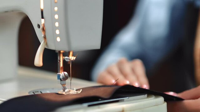 Female seamstress hands sews textile details use electric sewing machine mechanism closeup slowmo
