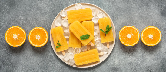 Orange popsicles border on gray background. Top view, flat lay, banner. Frozen orange juice on a...