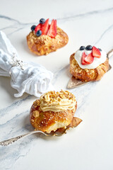 Three delicious buns with white sweet cream, nuts and berries. Sweet French pastries on a marble background