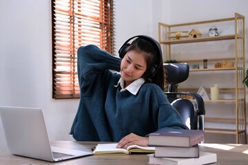 stressed Asian woman student learning from home is relaxing neck muscle to relieve strain while doing homework on the computer in the bedroom.