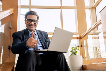 Indian businessman using laptop and showing thumps up at office
