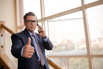 Indian businessman talking on smartphone and showing thumps up.