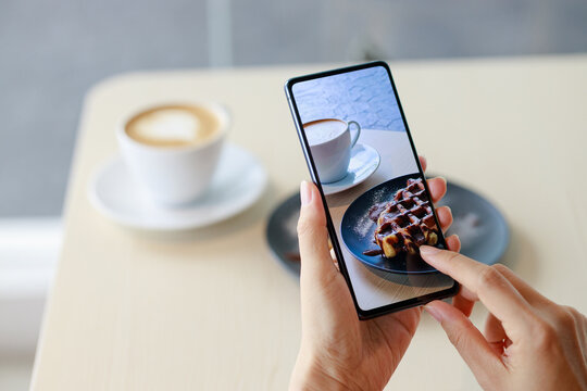 Female hands holding smartphone, taking photograph of her breakfast at a cafe. Concept of sharing food photo on social media.