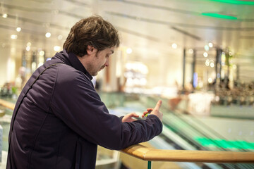 happy young unshaven man looking in smartphone in mall, horizontal