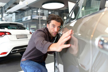 Car dealership - young handsome man check outside the quality of the new car paint