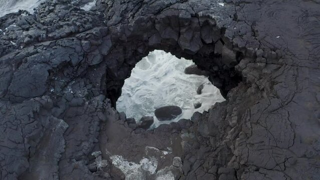 A Hole In The Volcanic Lava Rocks At The Shore Of Iceland. Aerial Pullback