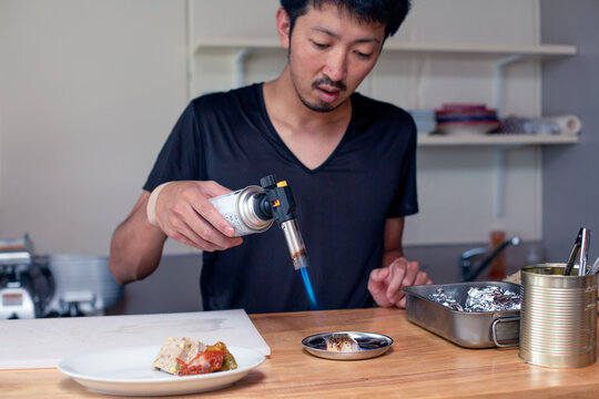 A chef preparing plates of Italian food in a restaurant. using a blow torch to heat a dish.
