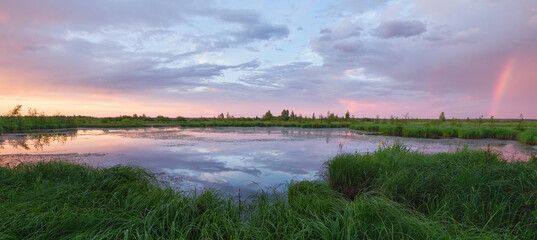 Colorful sunset and rainbow over swamp and forest: reflection of clouds, nature of Northern Europe,...