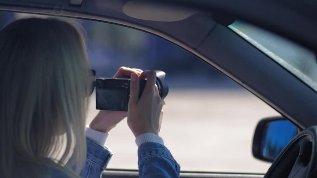 Paparazzi woman or girl sits in her car and takes pictures of famous person. Spy with camera in car. Private detective or paparazzi journalist sitting inside car, taking pictures with camera.