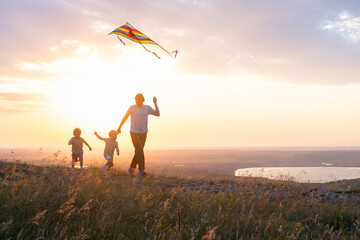 Happy man and children, father and sons, with kite in nature at sunset