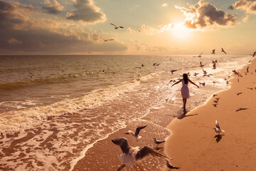 Seascape. Sunrise over the sea with a beautiful sky. Woman on the beach. Summer. Young happy woman with hands in the air walks along the seashore. Seagulls fly over the beach