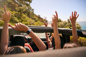 Group Of Laughing Female Friends Putting Hands Through Sunroof Open Top Car On Road Trip