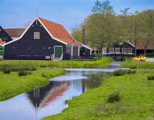 Fototapeta na wymiar Zaanse Schans, Netherlands - April 25, 2022: A tranquil residential district in Holland, Zaanse Schans is a beautiful landscape of grassy fields, trees and water featuring iconic Dutch architecture.