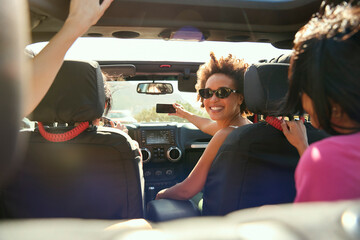 Laughing Female Friends Having Fun Posing For Selfie In Open Top Car On Road Trip