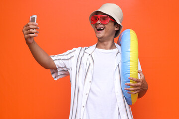 young traveler tourist man in summer clothes hat doing selfie shot on mobile phone while holding inflatable ring isolated on orange background