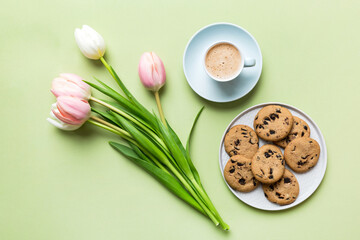 Cup of coffee mug with coffee, cookies and tulips on a colored background. Greeting spring card top view