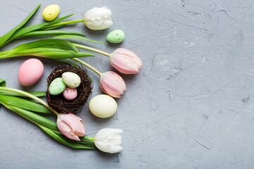 Happy Easter composition. Easter eggs in basket on colored table with yellow Tulips. Natural dyed colorful eggs background top view with copy space