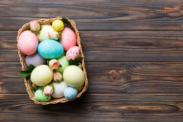 Happy Easter. Easter eggs in basket on colored table with yellow roses. Natural dyed colorful eggs background top view with copy space