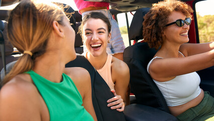 Group Of Laughing Female Friends Having Fun In Open Top Car On Road Trip