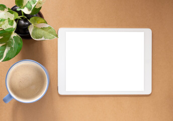 Obraz na płótnie Canvas Blank screen of tablet and coffee cup with plant on brwon workplace. Top view, flat lay with copy space. Template for business and education..