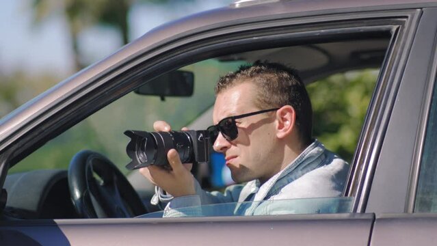 Paparazzi men or guy sits in her car and takes pictures of famous person. Spy with camera in car. Private detective or paparazzi journalist sitting inside car, taking pictures with camera.
