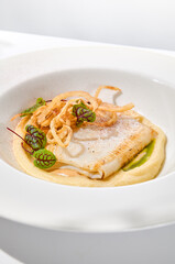 Roasted squid on mashed potatoes and crispy onion. Grilled squid with celery cream on white plate with shadows of leaves. Summer seafood menu. Roasted calamari in fine dining.