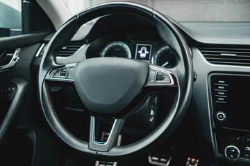 Modern black car interior, leather steering wheel, climate control, navigation, air ducts,...