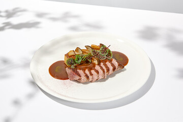 Roasted duck breast with potato gratin and sauce on light background. Fried duck fillet on white plate with hard shadows Elegant summer menu. French cuisine - duck breast with gravy