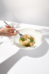 Woman hand holding fork with sea scallop over creamy risotto. Person eat seafood risotto with scallops. Female hand with italian risotto. Trendy menu concept.