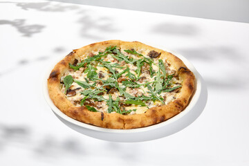 Mushroom pizza with cheese and arugula on white background with shadows. Italian pizza with porcini mushrooms on white table and hard shadows Cheese pizza in trendy style Modern italian food