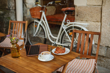 a laptop, a croissant with coffee on a table on the summer terrace in a cafe