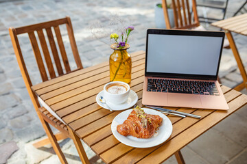 A laptop, croissant, and coffee on a cafe's summer terrace