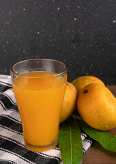 Fresh tropical fruit smoothie mango juice on wooden background with leaves and fruits.