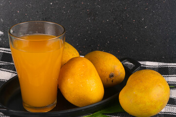 Fresh tropical fruit smoothie mango juice on wooden background with leaves and fruits.