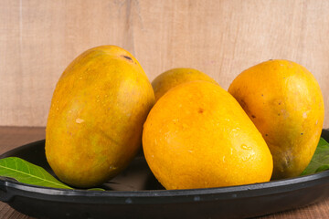 Ripe yellow Mango with cut in half and green leaf isolated on wooden background.