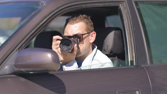 Paparazzi men or guy sits in her car and takes pictures of famous person. Spy with camera in car. Private detective or paparazzi journalist sitting inside car, taking pictures with camera.