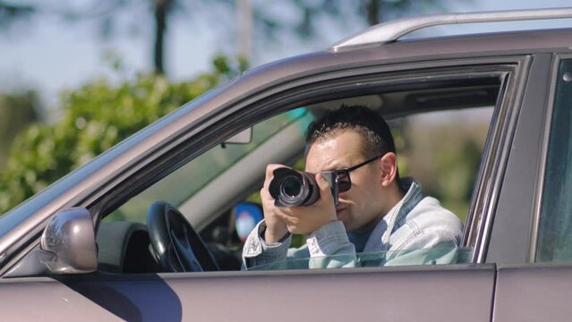 Man with camera sits inside car and takes pictures with professional camera, private detective or paparazzi spy. Journalist seeks synsation and follows celebrities.
