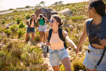 Fototapeta premium Group Of Female Friends With Backpacks Helping Each Other On Hike In Countryside On Coastal Path