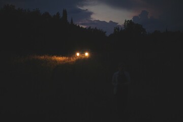 Woman walking on a field against a car with headlights on