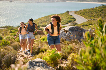 Group Of Female Friends With Backpacks On Vacation On Hike Through Countryside Next To Sea