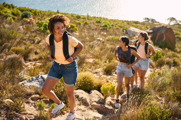 Group Of Female Friends With Backpacks On Vacation On Hike Through Countryside Next To Sea